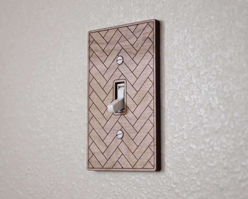 May include: A wooden light switch cover with a herringbone pattern. The switch is in the off position.
