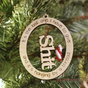 May include: A wooden Christmas ornament with the text "It's the last one I have to give and it's hanging by a thread" and the word "Shit" cut out in the center.