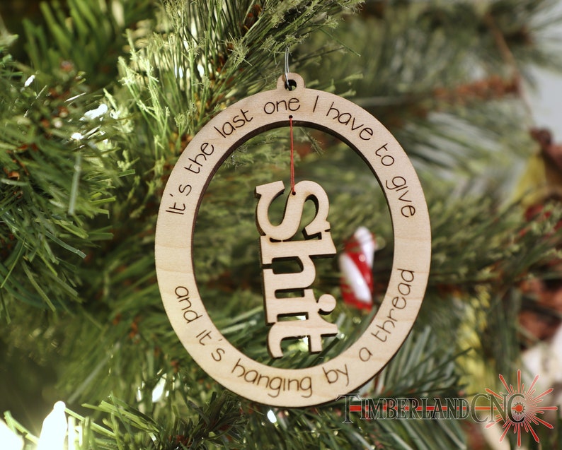 May include: A wooden Christmas ornament with the text "It's the last one I have to give and it's hanging by a thread" and the word "Shit" cut out in the center.
