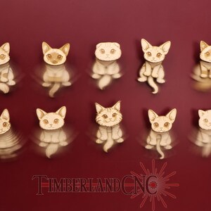 May include: Ten wooden cat figurines in various poses, each with detailed facial features and a light brown and white color scheme. The figurines are arranged on a deep red background. The text "TIMBERLAND CNC" is at the bottom.