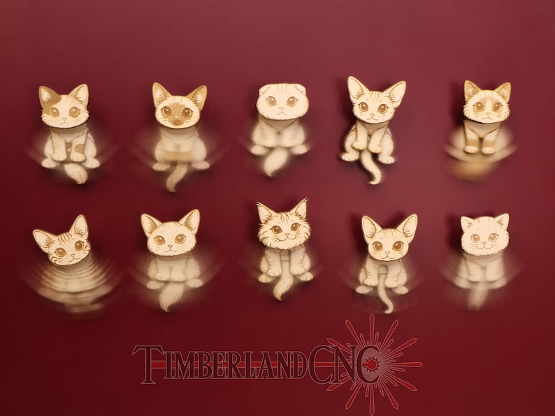 May include: Ten wooden cat figurines in various poses, each with detailed facial features and a light brown and white color scheme. The figurines are arranged on a deep red background. The text "TIMBERLAND CNC" is at the bottom.