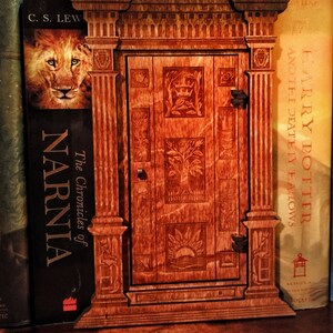 K&ouml;nnte beinhalten: Ein h&ouml;lzerner Buchst&uuml;tze in Form einer T&uuml;r mit aufwendigen Schnitzereien. Der Buchst&uuml;tze ist gegen ein Exemplar von "The Chronicles of Narnia" von C.S. Lewis und ein Exemplar von "Harry Potter and the Deathly Hallows" von J.K. Rowling gelehnt.
