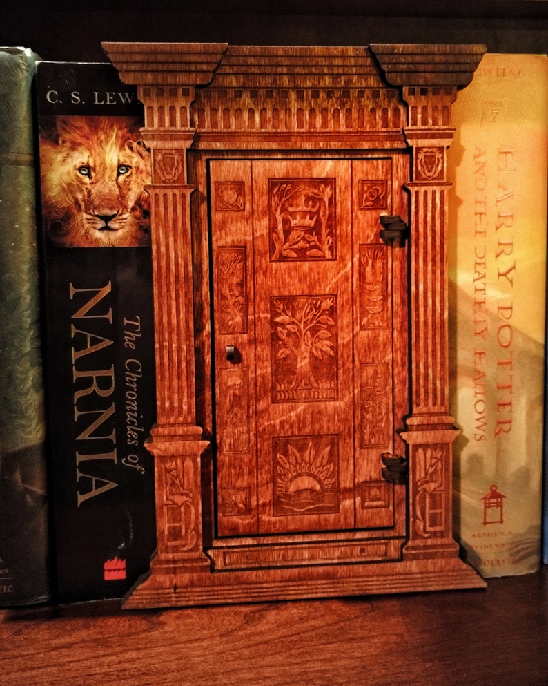 K&ouml;nnte beinhalten: Ein h&ouml;lzerner Buchst&uuml;tze in Form einer T&uuml;r mit aufwendigen Schnitzereien. Der Buchst&uuml;tze ist gegen ein Exemplar von "The Chronicles of Narnia" von C.S. Lewis und ein Exemplar von "Harry Potter and the Deathly Hallows" von J.K. Rowling gelehnt.