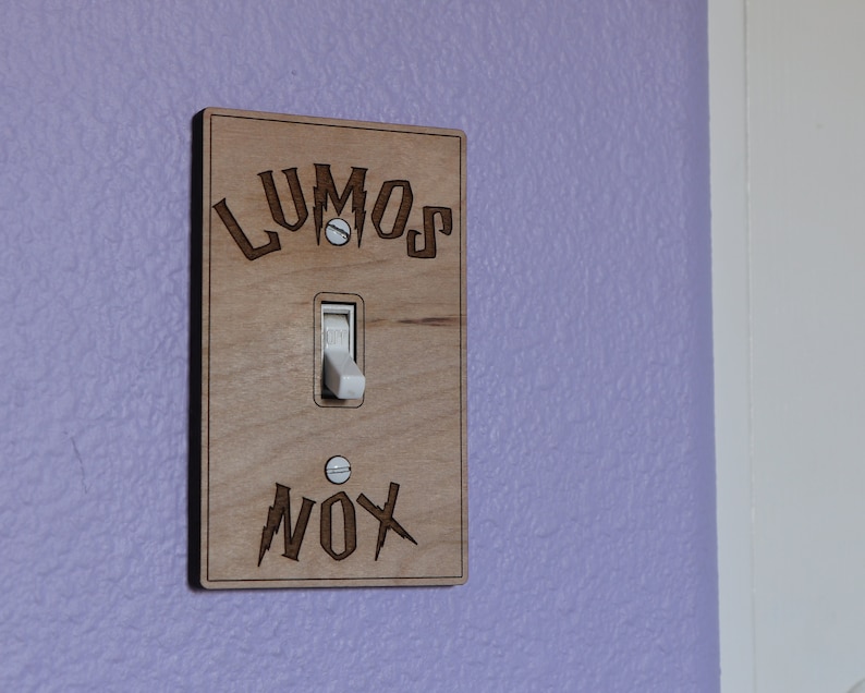 May include: A wooden light switch cover with the words "LUMOS" and "NOX" engraved on it. The switch is in the off position.