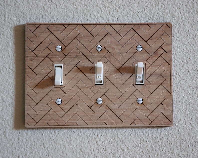 May include: A wooden light switch plate with a herringbone pattern and three toggle switches. The switches are white and have the word "ON" printed on them.