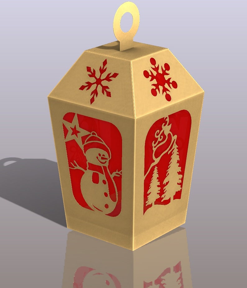 May include: A gold cardboard box shaped like a lantern with red cut-out designs of a snowman, snowflakes, and pine trees. The box has a loop at the top for hanging.