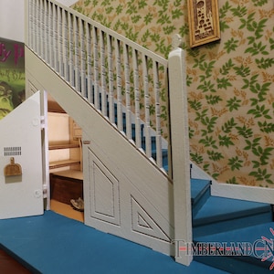 Op de afbeelding: Een witte houten trap met een geheime deur die leidt naar een kleine bergruimte. De deur staat open en laat planken en een kleine kamer zien. De trap heeft een blauw tapijt en een witte leuning. De muur achter de trap is bedekt met groen-gouden behang met een bloemenpatroon.