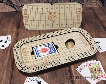 May include: A wooden cribbage board with a football field design. The board is engraved with the word "FOXES" and has a fox logo. The board is open and a deck of cards is visible.