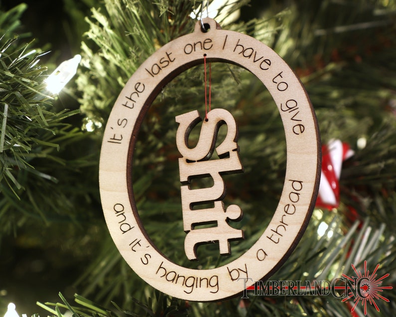 May include: A wooden Christmas ornament with the text "It's the last one I have to give and it's hanging by a thread" and the word "SHIT" cut out in the center.