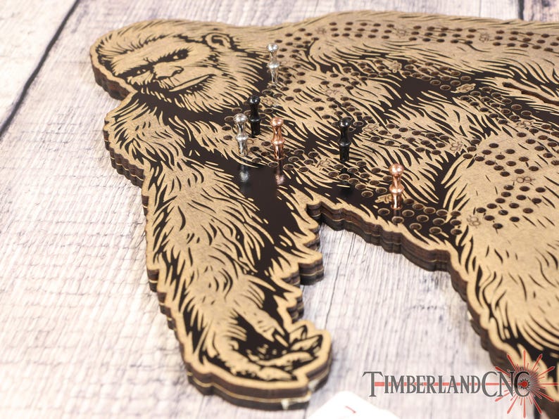 May include: A wooden game board shaped like a Bigfoot with a black and brown design. The board has a grid of holes and is decorated with metal pins.