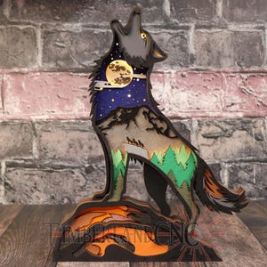 May include: A wooden cutout of a wolf howling at the moon, with a layered design featuring a starry night sky, mountains, and trees. The wolf is painted in shades of gray, black, and brown, with accents of green and blue.