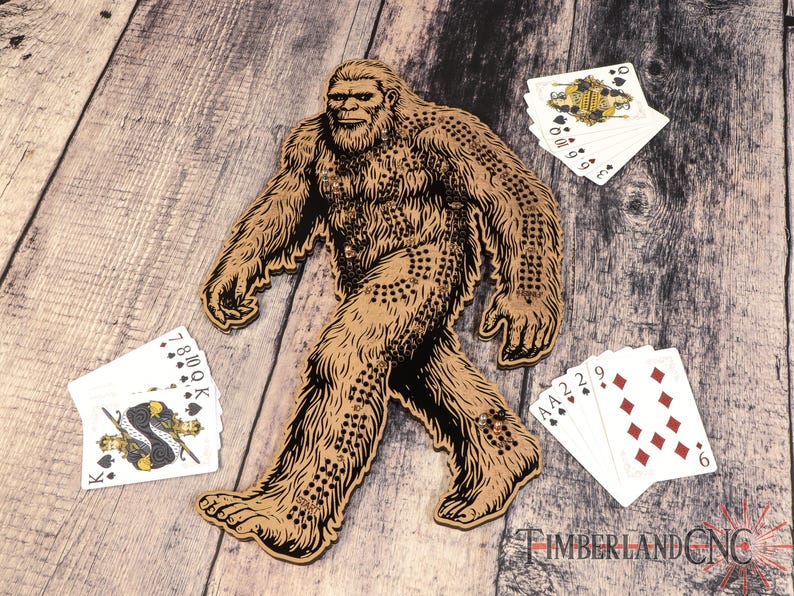 May include: A wooden Bigfoot cutout with a brown and black design. The cutout is surrounded by playing cards with various suits and numbers.
