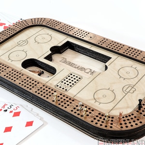 Può includere: Un tabellone da cribbage in legno con un design da pista di hockey. Il tabellone ha una finitura nera e marrone e presenta un tabellone segnapunti, una sezione 'vittorie' e una pista per i pioli. Il tabellone è realizzato da TimberlandCNC.