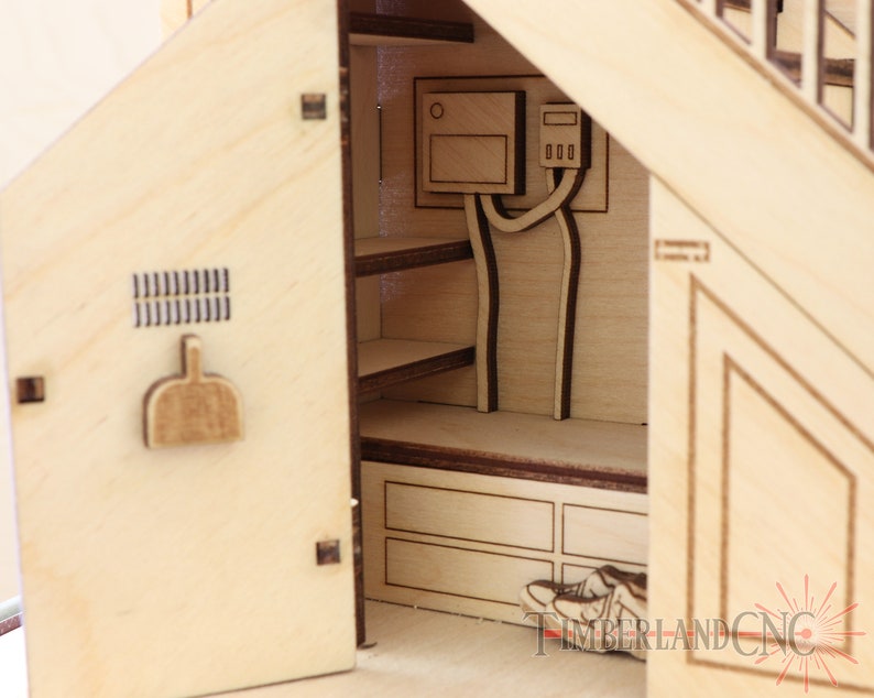 Op de afbeelding: Een houten model van een huis met een open deur die een kleine binnenruimte onthult. De binnenruimte heeft planken, een klein bankje en een deur met een klein raam. Het model is gemaakt van licht hout en heeft een natuurlijke afwerking.