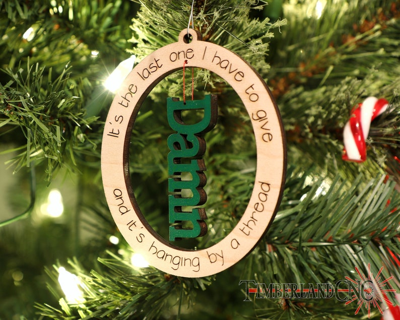 May include: A wooden Christmas ornament with the text "It's the last one I have to give and it's hanging by a thread" and the word "Damn" in green letters.