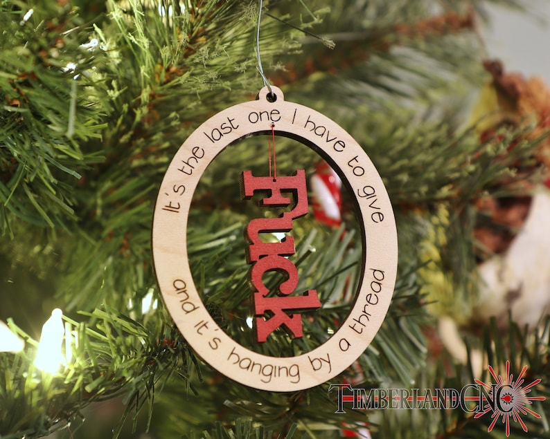 May include: A wooden Christmas ornament with the text "It's the last one I have to give and it's hanging by a thread" and the word "F*ck" in red letters inside a circle.
