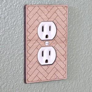 May include: A wooden wall plate with a herringbone pattern and two standard electrical outlets.