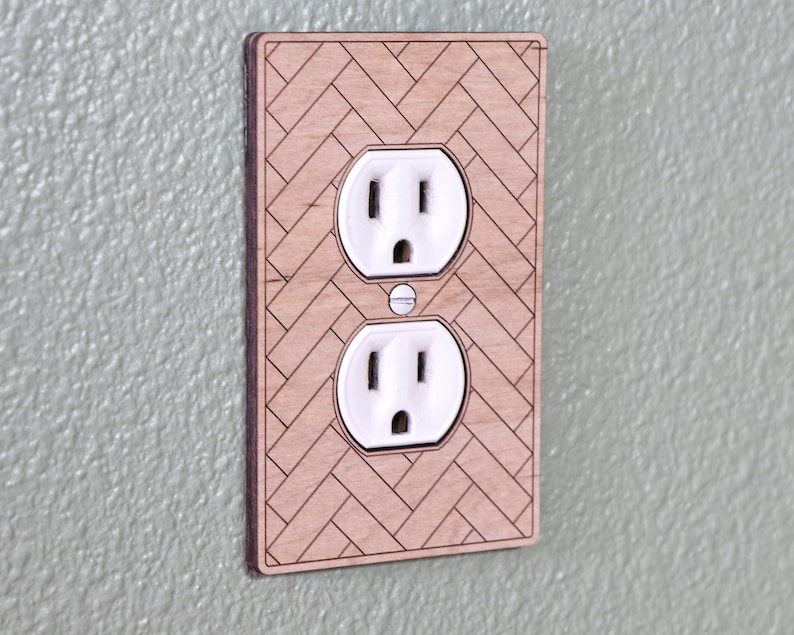 May include: A wooden wall plate with a herringbone pattern and two standard electrical outlets.