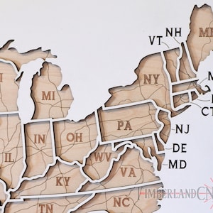 May include: A wooden map of the United States with each state outlined and labeled. The map is made of light brown wood with white outlines. The states in the Northeast are highlighted.