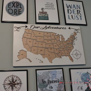 May include: A wooden map of the United States with a compass and the words "Our Adventures" above it. The map is surrounded by framed prints with travel-themed text, including "Explore", "Let's go somewhere anywhere everywhere", and "Wanderlust".