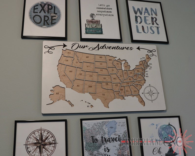 May include: A wooden map of the United States with a compass and the words "Our Adventures" above it. The map is surrounded by framed prints with travel-themed text, including "Explore", "Let's go somewhere anywhere everywhere", and "Wanderlust".