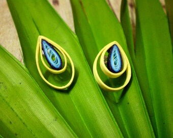 May include: A pair of yellow and blue paper quilled earrings in the shape of teardrops. The earrings are layered with blue and white paper quills and are set against a green leaf background.