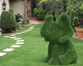 May include: A green topiary sculpture of a dog sitting on a green lawn with a stone path leading to a house in the background.