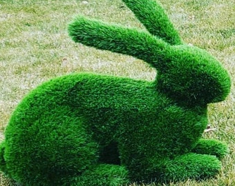 May include: A green, grass-like rabbit sculpture. The sculpture is made of artificial grass and is sitting on a green lawn.