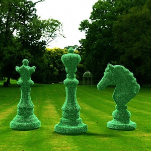May include: Three large green topiary chess pieces, a king, a queen, and a knight, are arranged on a grassy lawn. The pieces are made of trimmed bushes and are shaped like traditional chess pieces.