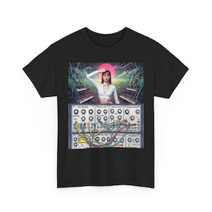 Puede incluir: Camiseta negra con un gráfico colorido. El gráfico representa a una mujer pelirroja con un top blanco, frente a un sintetizador. El sintetizador tiene muchas perillas y cables coloridos. El fondo incluye teclados y un sol rosa.