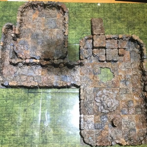 Könnte beinhalten: Ein Set aus zwei braunen und grauen, steintexturierten Dungeon-Kacheln für Tabletop-Spiele. Die Kacheln sind aus einem strapazierfähigen Material gefertigt und weisen eine Vielzahl von Texturen und Details auf, darunter Wände, Böden und ein Loch in der Mitte einer Kachel.