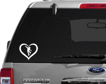 May include: A white silhouette of a dancer in a heart shape decal on the back window of a silver SUV. The SUV has a black rear window and a black rear bumper.