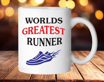 Puede incluir: Taza de café de cerámica blanca con el texto "Worlds Greatest Runner" en letras negras y rojas. Un zapato de correr azul con llamas está impreso debajo del texto.