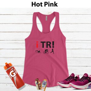 May include: Hot pink racerback tank top with the text "i TR!" and triathlon icons. Includes a red and orange water bottle, two energy gel packets, and a pair of pink and black athletic shoes.