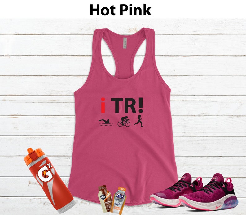 May include: Hot pink racerback tank top with the text "i TR!" and triathlon icons. Includes a red and orange water bottle, two energy gel packets, and a pair of pink and black athletic shoes.