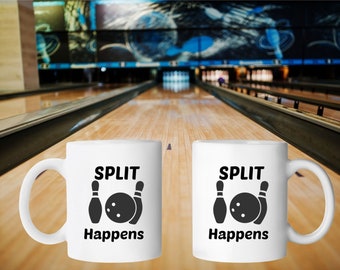 Puede incluir: Dos tazas de cerámica blanca con asas negras. Ambas tazas tienen un gráfico negro de bola y bolos de bolos con el texto "SPLIT Happens". Las tazas están sobre una superficie de madera frente a un fondo borroso de una bolera.