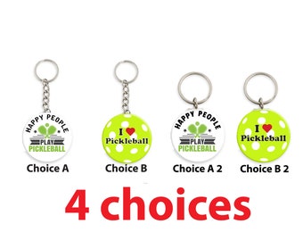 Puede incluir: Cuatro diseños diferentes de llaveros de pickleball. Dos llaveros presentan un círculo blanco con texto negro que dice "Happy People Play Pickleball" y una pala de pickleball verde. Los otros dos llaveros presentan un círculo verde lima con puntos blancos y texto negro que dice "Me encanta el pickleball" con un corazón rojo.