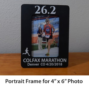 May include: Black wooden picture frame with a white runner silhouette, the text "26.2 COLFAX MARATHON Denver CO 4/20/2018", and a photo of a runner in the frame. The frame is designed to hold a 4 inch by 6 inch photo.