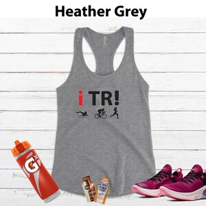 May include: Heather grey racerback tank top with "i TR!" text and triathlon icons. Includes a red and orange water bottle, energy gel packets, and magenta running shoes.