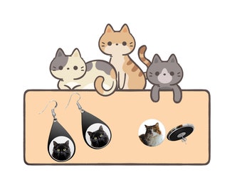 Puede incluir: Un juego de pendientes con temática de gatos. Un par presenta un gato negro con ojos verdes en un diseño en forma de lágrima. El otro par presenta un gato marrón y blanco en un diseño redondo. Los pendientes se muestran sobre un fondo marrón claro con gatos de dibujos animados.