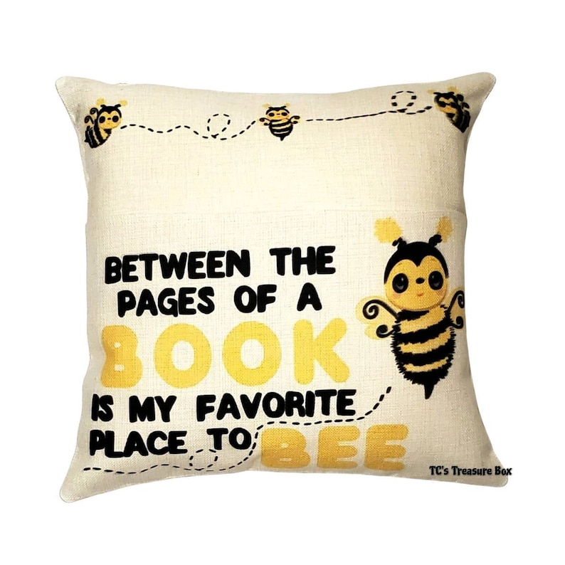 May include: A beige throw pillow with a yellow and black bee illustration and the text "Between the pages of a book is my favorite place to bee".