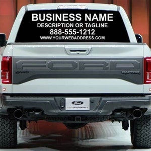 May include: A white Ford Raptor pickup truck with a black rear window decal. The decal includes the text "BUSINESS NAME", "DESCRIPTION OR TAGLINE", "888-555-1212", and "WWW.YOURWEBADDRESS.COM".
