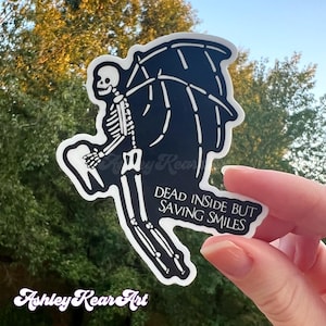 May include: Black and white sticker featuring a skeleton with wings holding a tooth. The text "Dead inside but saving smiles" is written below the skeleton.