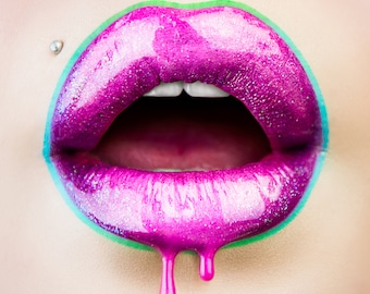 May include: Close-up of open lips with vibrant, glossy magenta lipstick. The lips are outlined in teal and green, with a silver lip piercing. The lipstick drips down, creating a bold and artistic effect. The image is a beauty and fashion statement.