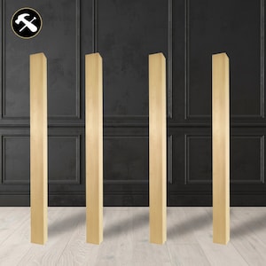 May include: Four wooden columns, each standing upright against a black wall with white trim. The columns are a light wood color and are all the same size.