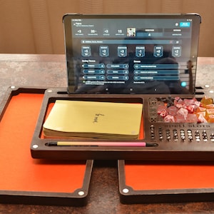 Peut inclure: Un plateau de jeu en bois avec une surface recouverte de feutre, un support pour tablette, un compartiment pour les dés et une section pour les emplacements de sorts. Le plateau est brun avec un revêtement en feutre orange. Le support de tablette est vide et le compartiment à dés est rempli de dés de différentes couleurs.