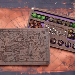 Könnte beinhalten: Würfelablage und Karte aus Holz. Die Ablage hat Schlitze für Würfel und den Text "spell slots". Die Karte ist mit einem detaillierten Design graviert. Die Würfel sind in verschiedenen Farben, darunter Grün, Braun und Gold.