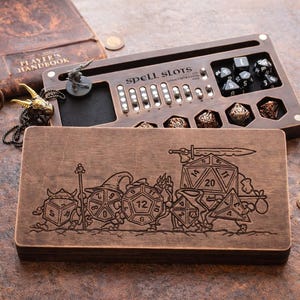Könnte beinhalten: Würfelspiel-Tablett und Aufbewahrungsbox aus Holz mit dem Text "spell slots". Das Tablett hat Schlitze für Würfel und eine kleine Figur. Die Box ist mit einem Fantasy-Design graviert. Eine Kerzenlaterne und ein Buch befinden sich im Hintergrund.