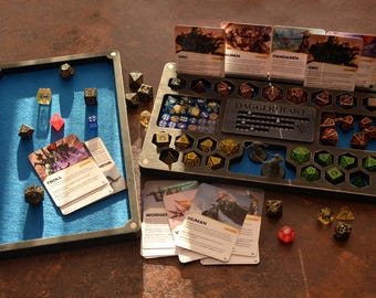 Op de afbeelding: Een tabletop-gameset met dobbelstenen, kaarten en organizers. De set bevat een met blauw vilt gevoerde lade, een dobbelsteenhouder met diverse compartimenten en karakterkaarten. Dobbelstenen zijn in diverse kleuren en vormen.
