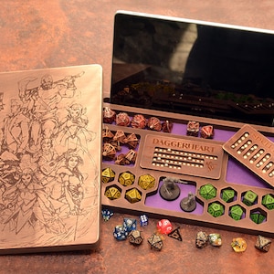 Op de afbeelding: Een houten Daggerheart-spelorganizer met een paarse binnenkant, voorzien van een deksel gegraveerd met fantasiefiguren, een spellenslot-tracker en diverse veelzijdige dobbelstenen in gele, groene en metallic tinten, naast twee kleine miniaturen.